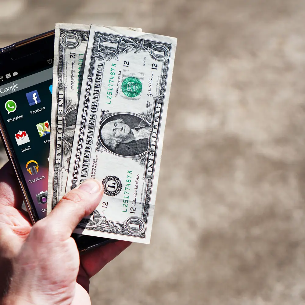 Celular y dólares que representan los métodos para retirar dinero de OnlyFans en Argentina